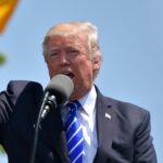 Donald Trump speaking passionately at a podium, emphasizing branding advice for Boeing's 737 MAX, with American flags in the background.
